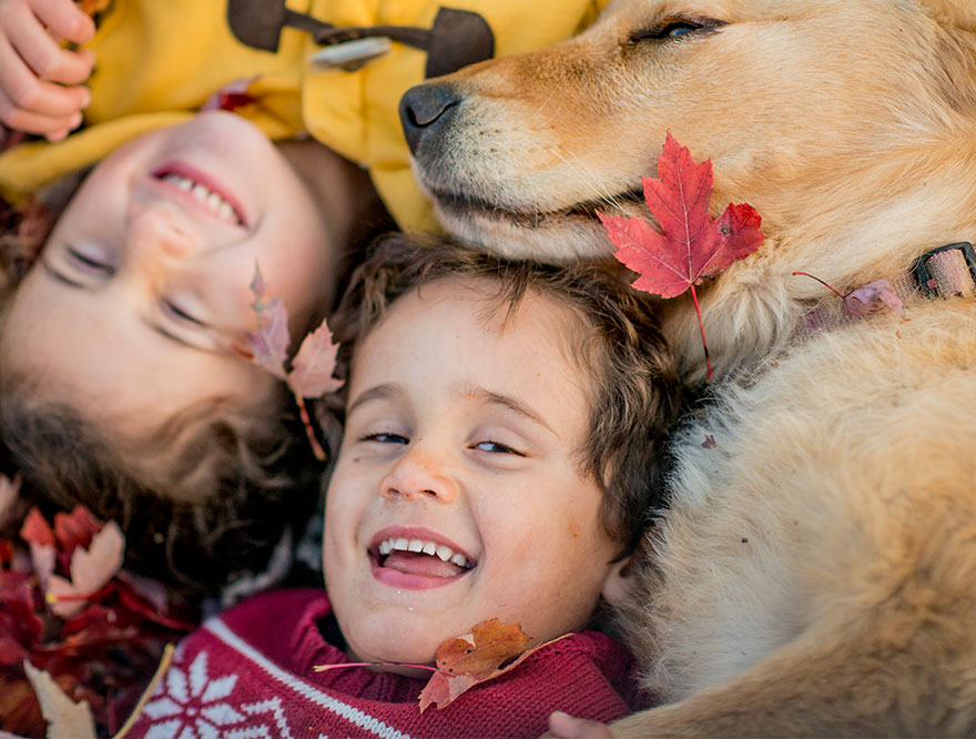 two kids laying in leaves with a dog