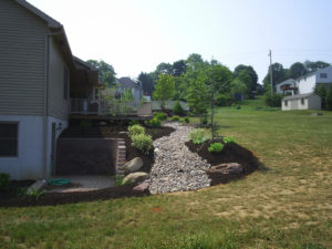 freshly installed stone and mulch beds leading down a hill next to a retaining wall and basement entrance