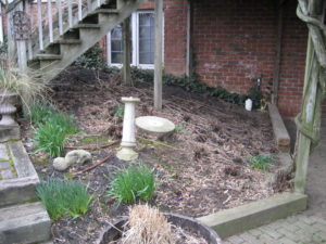 An old mulch bed filled with debris, a broken bird bath and a few liriope