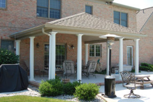 a covered backyard porch with patio furniture and stone mulch bed