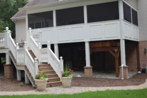enclosed backyard deck with staircase leading down to hardscaped paver walkway