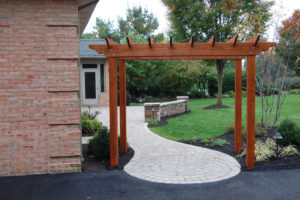 brown pergola and paver walkway next to a driveway