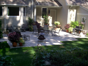 shaded backyard paver patio with potted plants, patio furniture, a grill, a golden retriever and more
