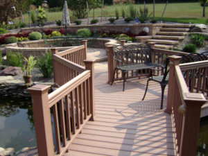 a bridge over a built in pond that leads to hardscaped patio seating area with patio furniture