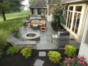 backyard patio after a rain. a grill, fire pit, furniture, planters and hot tub can all be seen
