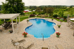 an amazing pool surrounded by hardscaped pavers, flower pots, a pergola and a seating area