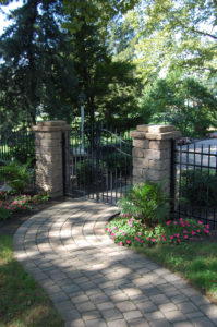curving paver patio leading to a black gate between two pillars
