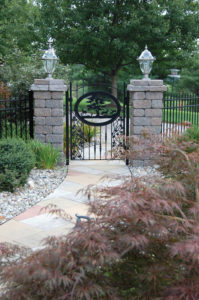 hardscaped walkway leading to a decorative black gate between two stone pillars