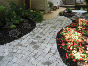 hardscaped paver walkway next to two flowerbeds with blooming flowers