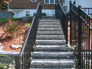 stone walkway with railing leading up to a home between flower beds
