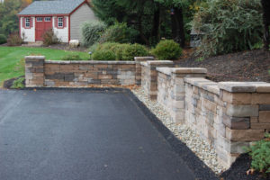 freshly paved driveway with stone retaining wall and pillars. a shed sits in the background