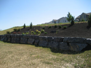 large stone retaining wall with black mulch bed and new shrub plantings
