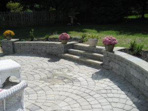 decorative stone patio in front of a stone wall with flower planters on it