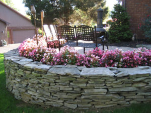 stone wall with blooming flowers and stone patio above