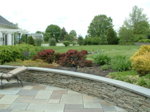 paver patio with stone wall and a large mulch bed