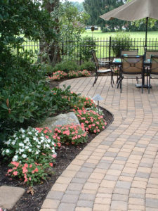 hardscaped patio next to a black mulch bed that has flowers, a stone and other shrubs