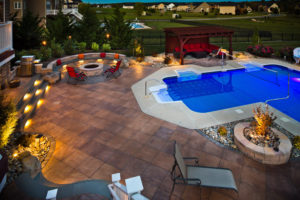 pool area professionally hardscaped, with a fire pit and seating area in the background