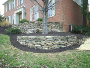 2 levels of stone wall and mulch beds in front of a brick home.