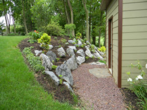 red stone mulch leads to a garage door. a mulch bed with large stones leads down a hill to the red stone