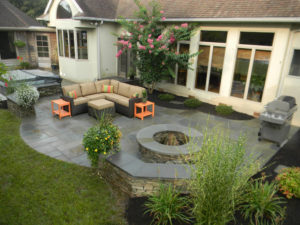 a slate patio after a rain. outdoor furniture sits near a fire pit and grill