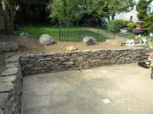 a stone wall in the corner of a patio, next to steps.