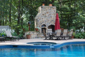 a beautiful outdoor fireplace beyond a pool and spa.