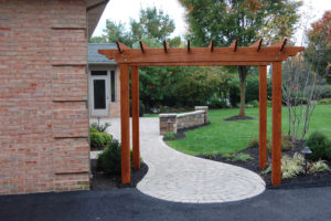 a wooden pergola and paver walkway/patio leading to a backdoor