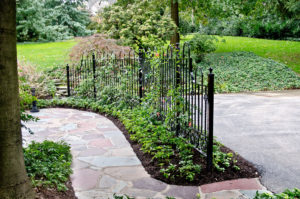 a small black fence separates a driveway and stone walkway