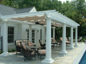 a large shade structure providing shade to a backdoor entrance and seating area next to a pool.