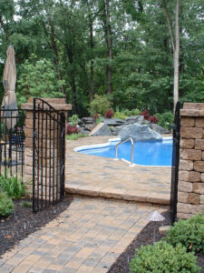 a paver walkway leading in through a gate to a paver patio surrounding a pool