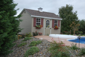 a pool house beside a pool and spa. stone mulch and evergreens slope downhill next to the pool house
