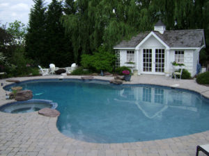 an outdoor pool and spa. a fire pit seating area and pool house are in the background