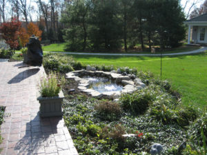 hardscaped paver patio next to a mulch bed and small pond