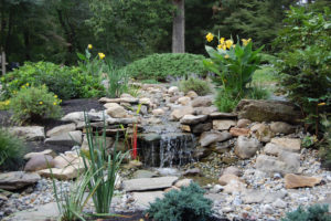 stone waterfall surrounded by black mulch beds, flowers, shrubs, and trees