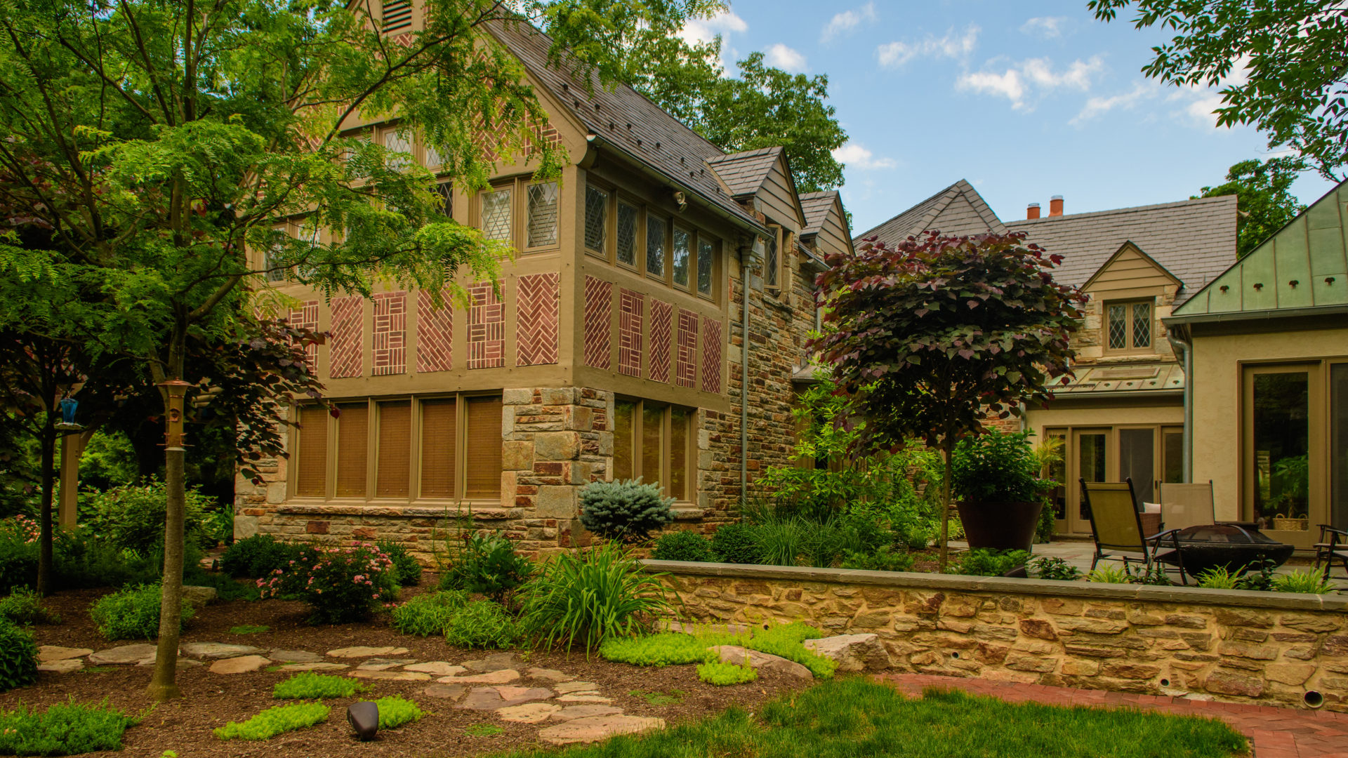 trees, shrubs, stone wall, stone patio and more in the backyard of a home